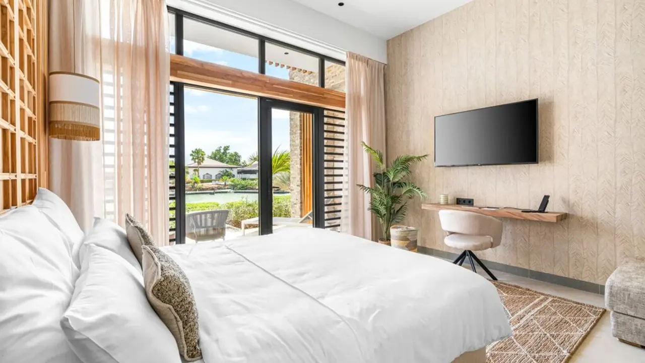 Deluxe Room Laguna van Van der Valk Bonaire met bed, televisie en uitzicht op het water door de pui