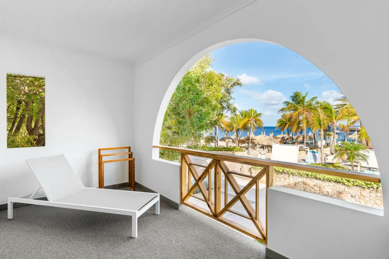 Balkon van de King Suite Ocean van Van der Valk Bonaire met ligbed en uitzicht op zee door een boog