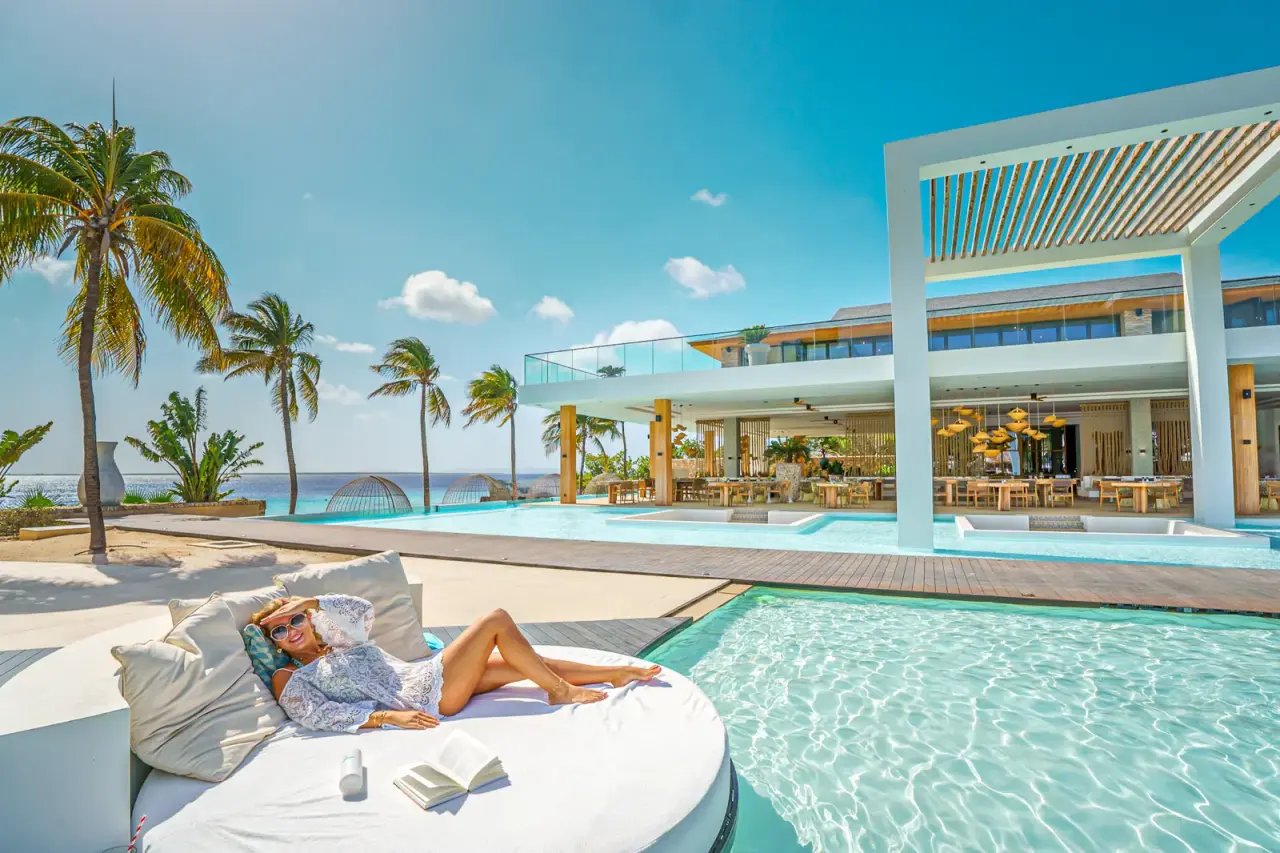 Rond loungebed aan het zwembad van Van der Valk Bonaire met palmbomen en zee